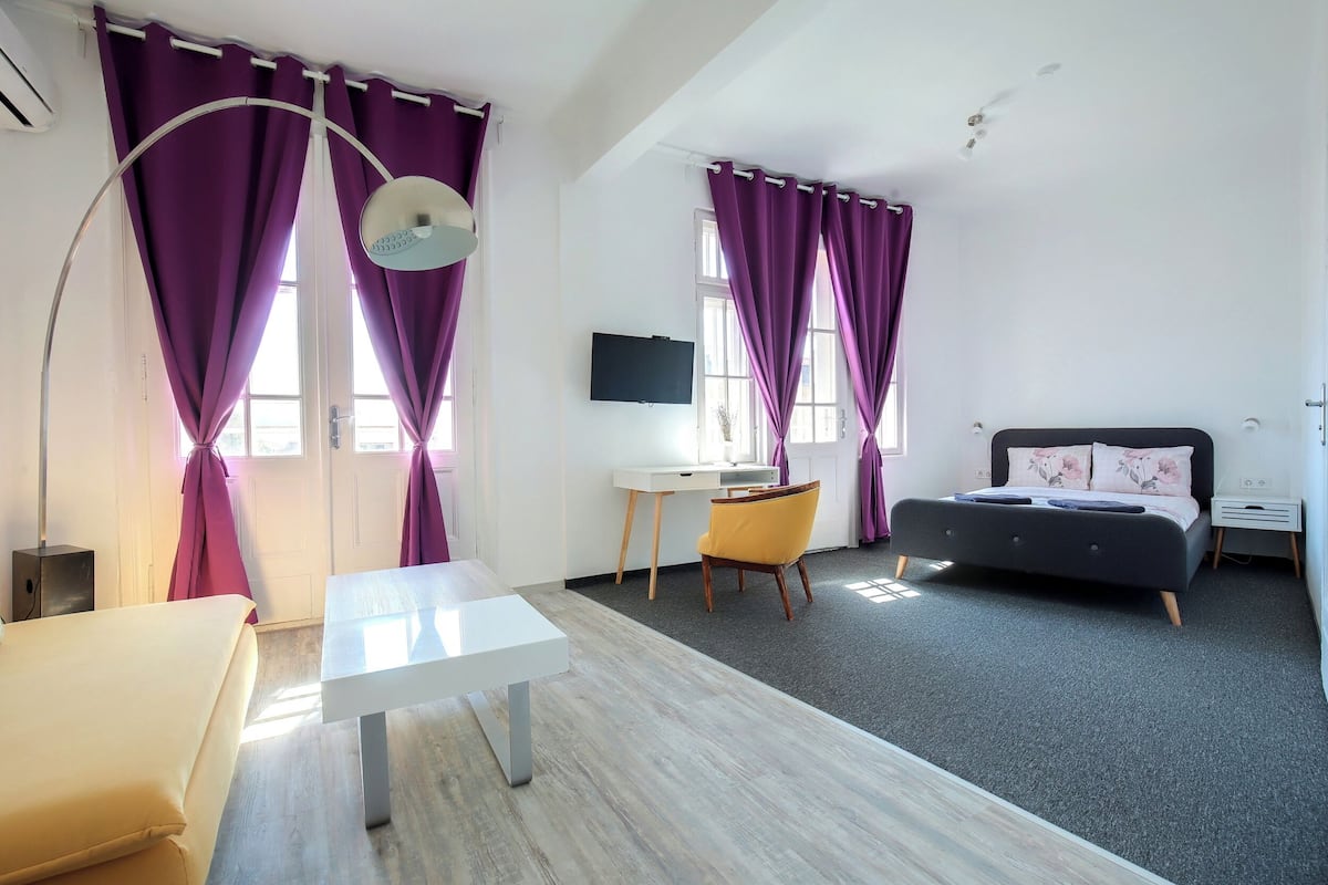 A modern bedroom with a bed, desk, chair, and a TV.