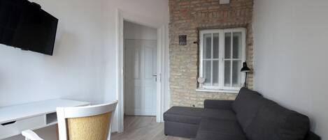 A living room with a white desk, a grey sofa, and a brick wall.