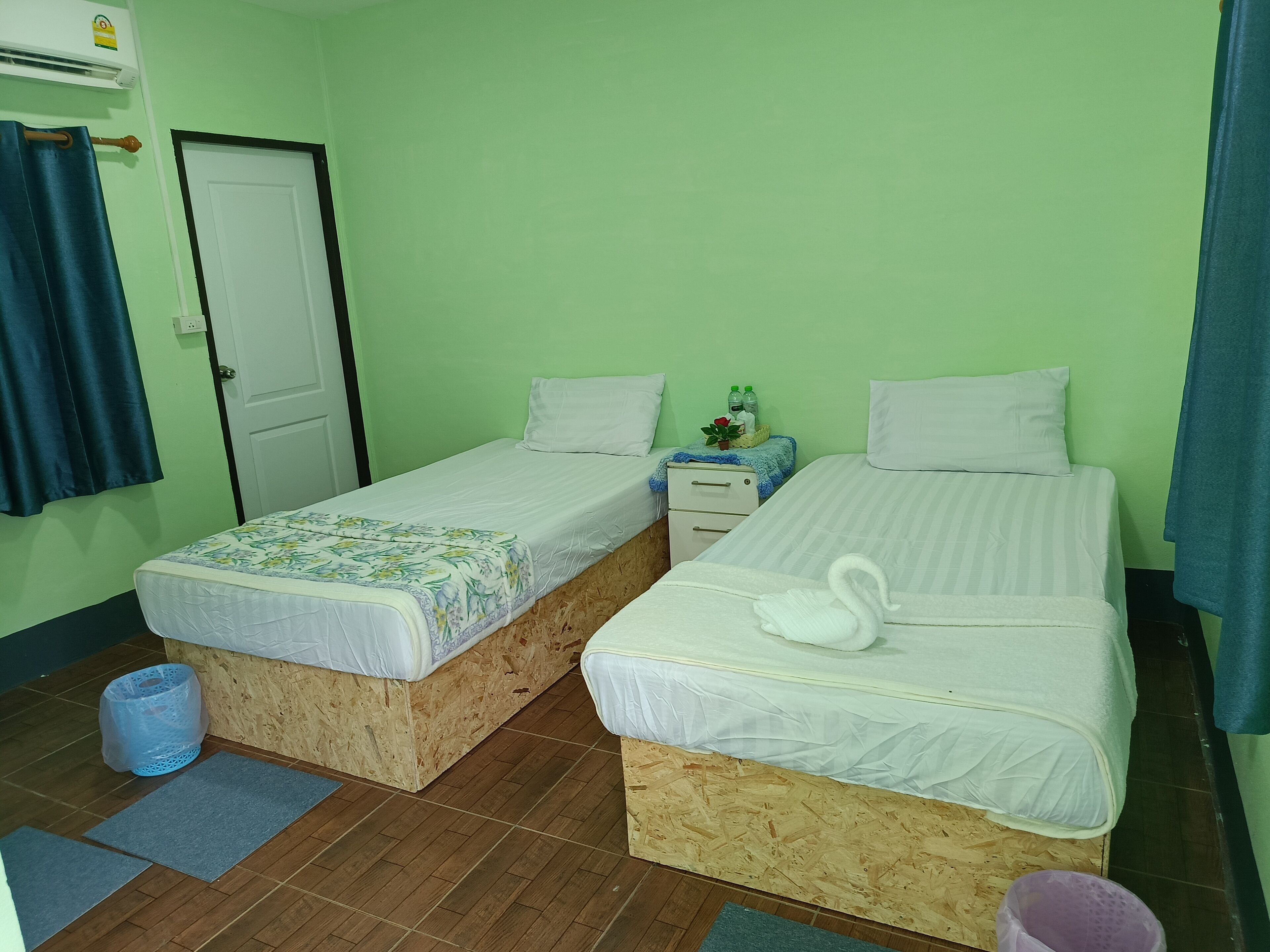 A room with two wooden bunk beds, a small bedside table with a lamp, a door, and a window with curtains.