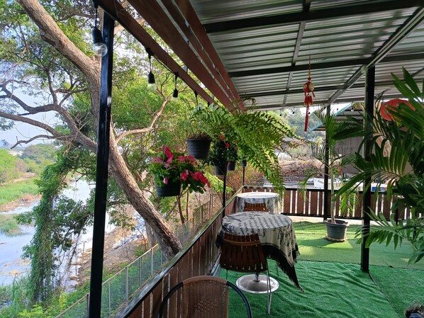 A covered outdoor area with a table and chairs, potted plants, and a view of a river.