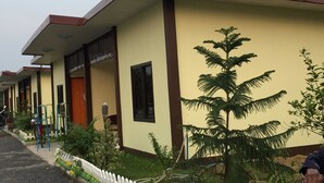 A row of single-story buildings with a flat roof and a beige exterior. Each building has a door and windows, and there is a small garden area with plants and a white picket fence in front. - Bussaracum Hotel (Tha Muang)