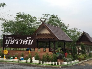 A traditional Thai house with a signboard, surrounded by greenery and a white picket fence.