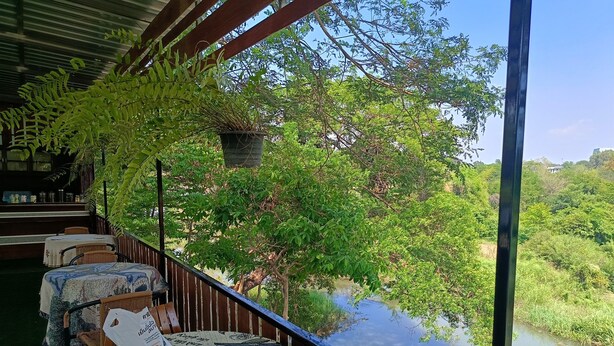 A balcony with wicker chairs and a table, overlooking a river and lush greenery.