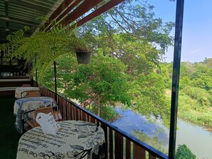 En balkon med fletstole og et bord, der giver udsigt over en flod og frodig vegetation.