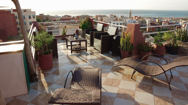 Eine Dachterrasse mit Gartenmöbeln, Blumentöpfen und Blick auf Stadt und Meer.