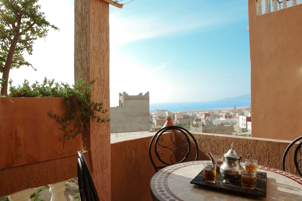Ein Balkon mit einem für Tee gedecktem Tisch, mit Blick auf die Stadt und das Meer.