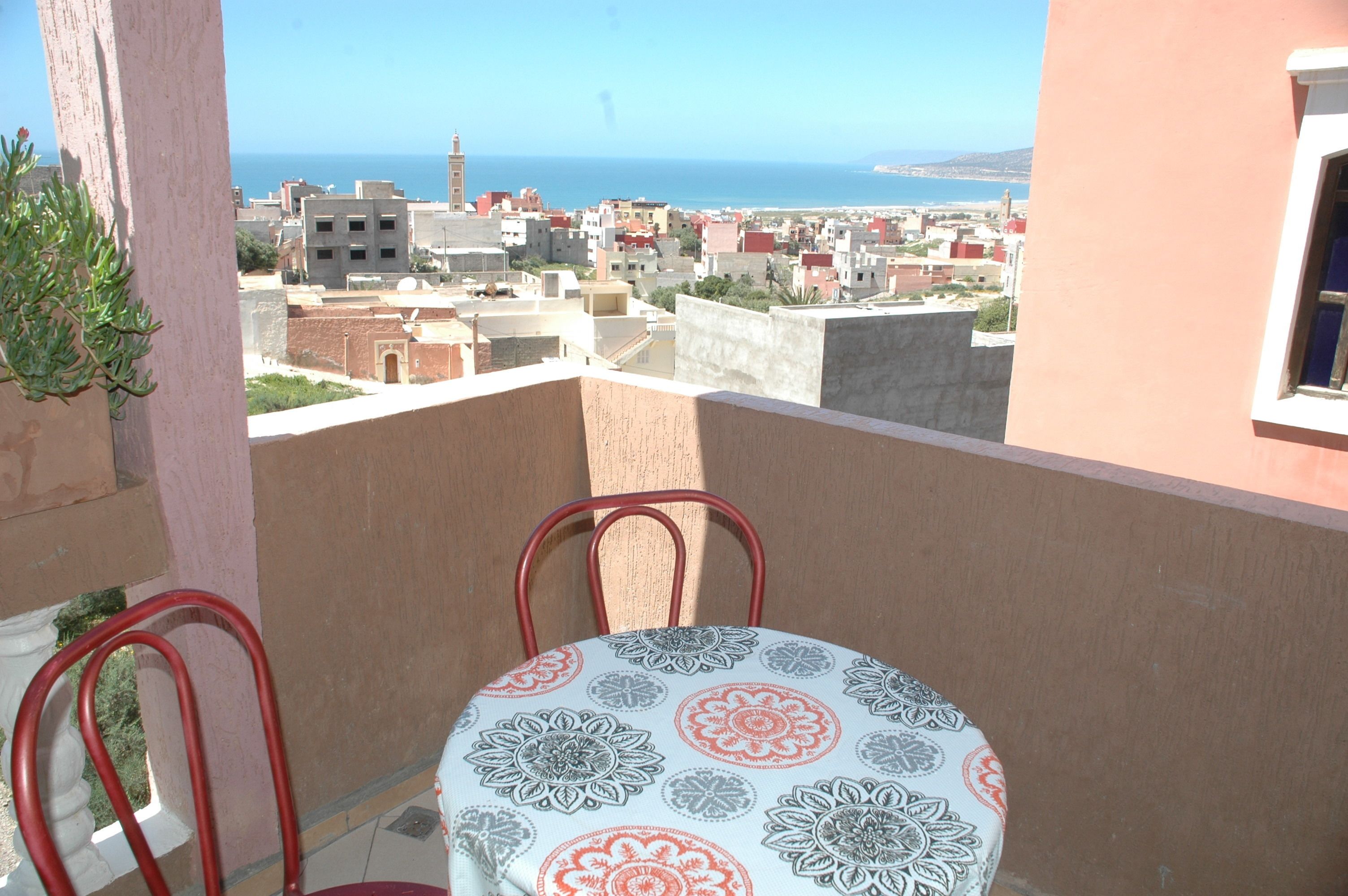 A balcony with a table and chairs, overlooking a coastal cityscape with buildings and a lighthouse.