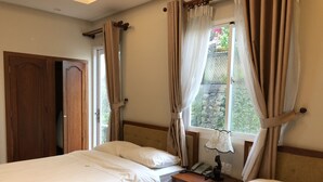 Habitación de hotel con dos camas, cabecero de madera, mesita de noche con lámpara, teléfono y ventana con cortinas.