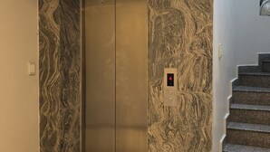 Un ascensor con diseño de pared de mármol, una pantalla digital y una escalera con peldaños de granito.