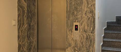 An elevator with a marble wall design, a digital display, and a staircase with granite steps.