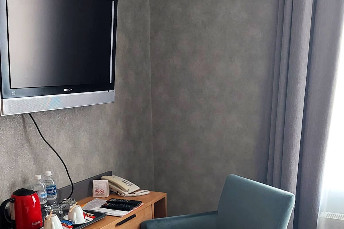 A hotel room with a flat-screen TV mounted on the wall, a wooden desk with a telephone, a red coffee maker, and a blue armchair.