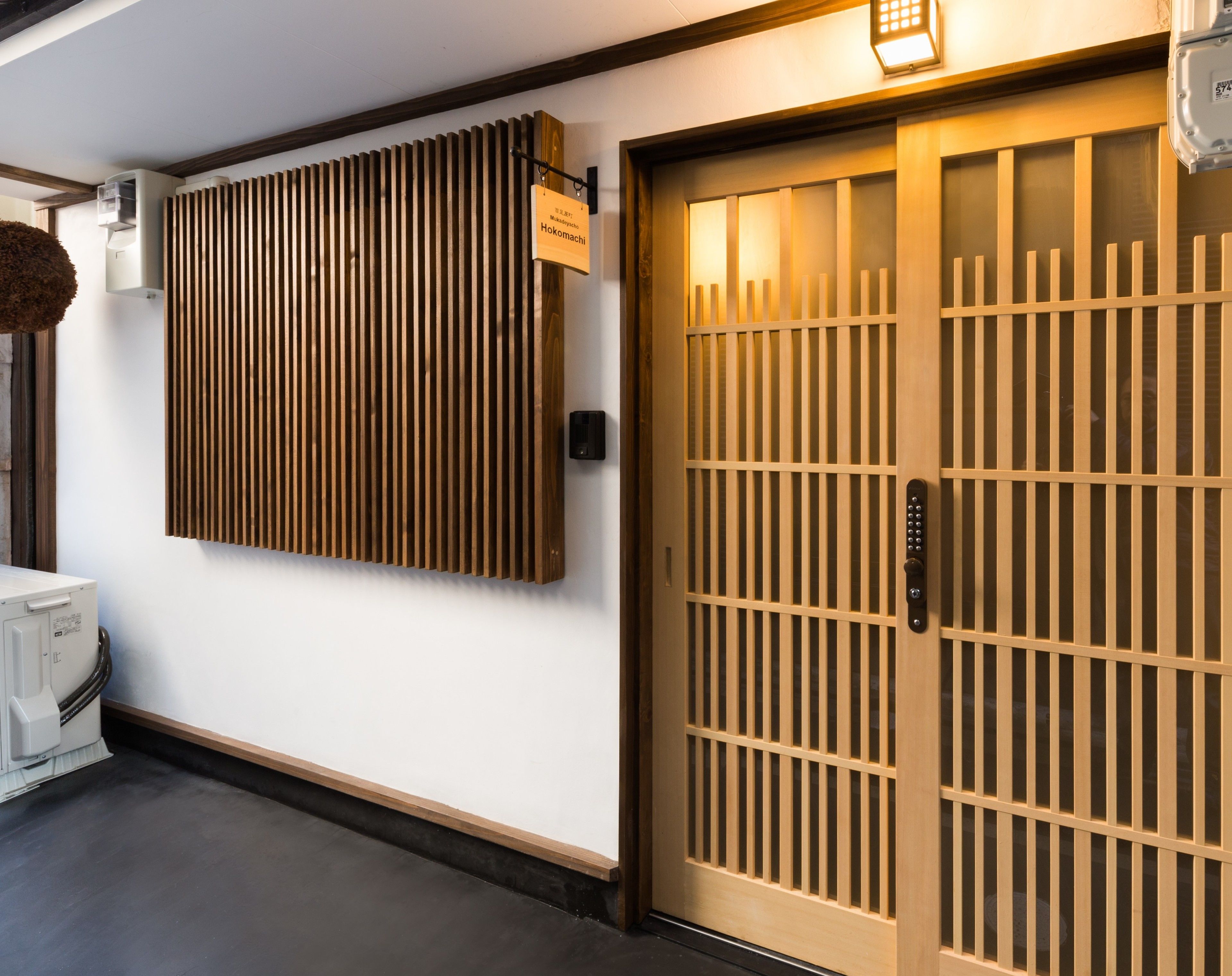 A traditional Japanese-style entrance with a sliding wooden door and a vertical wooden panel on the wall.