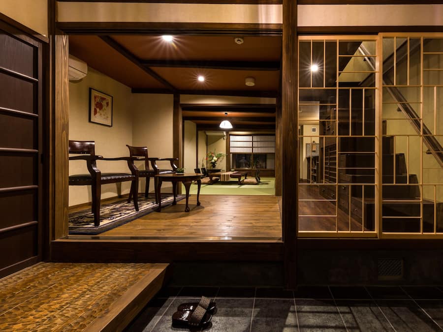 A traditional Japanese interior with tatami flooring, wooden furniture, and a sliding door leading to a staircase.