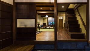 A traditional Japanese interior with a wooden staircase, tatami mat flooring, and a sliding door leading to a living area with a low table and chairs. - Kyoisuke (Kyoto)