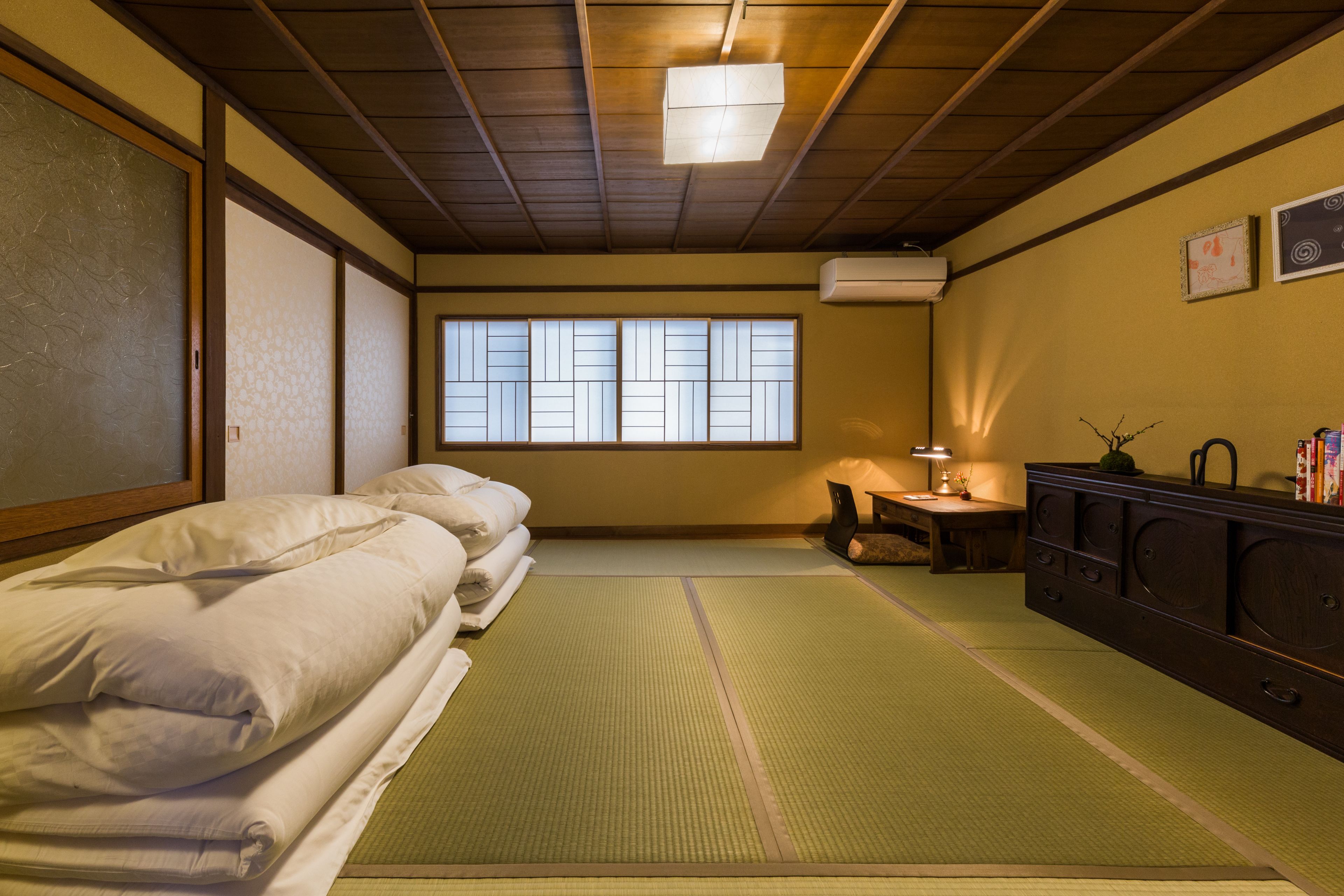 Et traditionelt japansk rum med tatamimåtter, en lav træseng, et lille bord med en lampe og et skab.