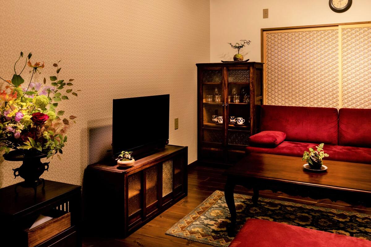 Ein traditionelles japanisches Wohnzimmer mit einem roten Sofa, einem Holztisch, einem Fernseher und einem dekorativen Schrank.