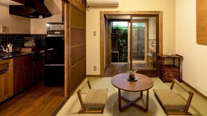 A compact kitchen with wooden cabinets, a refrigerator, and a dining area with tatami mats and a small table. - Kyoisuke (Kyoto)