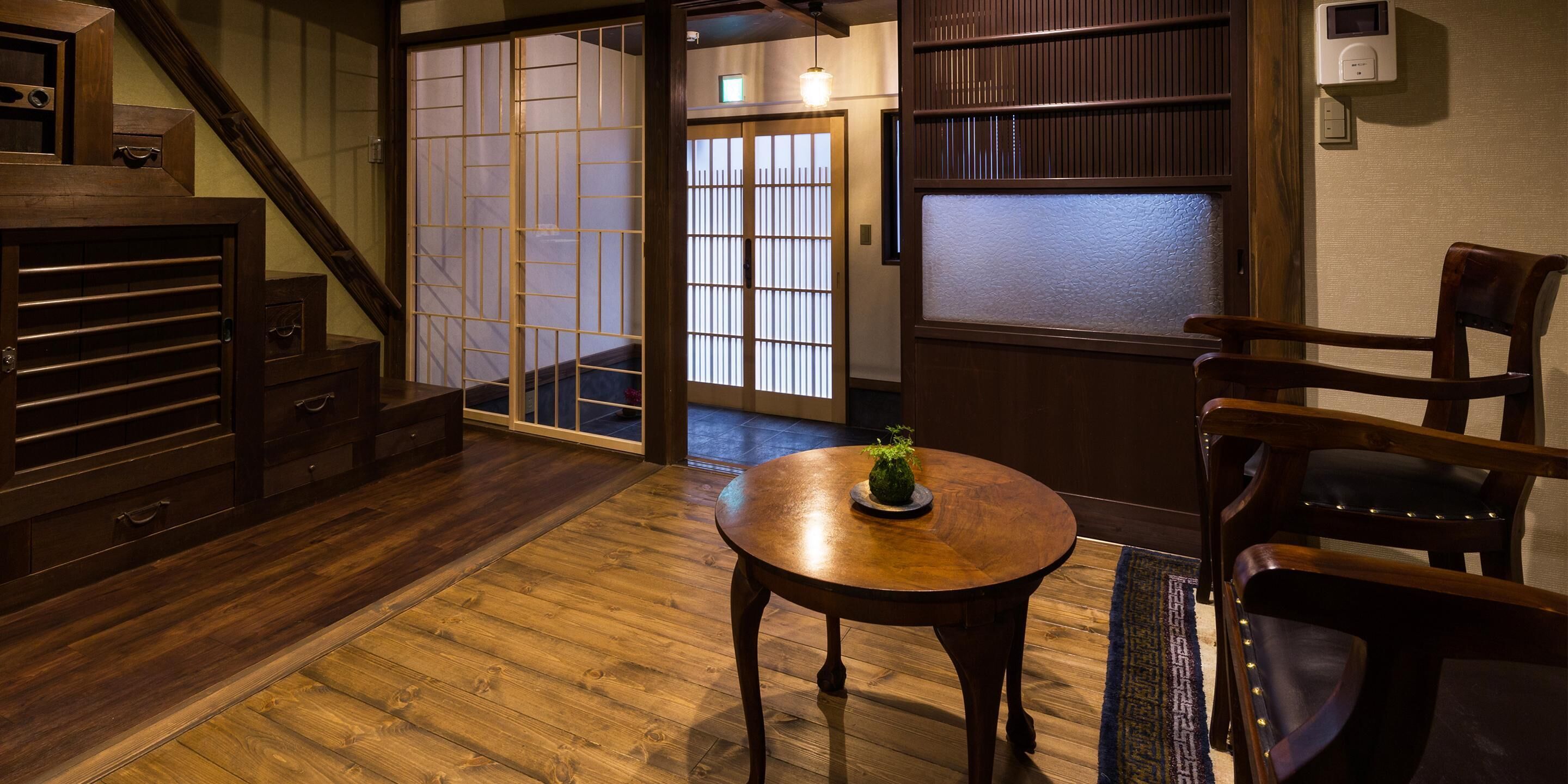 A traditional Japanese-style room with a wooden floor, sliding doors, a small round table with a plant, and a chair.