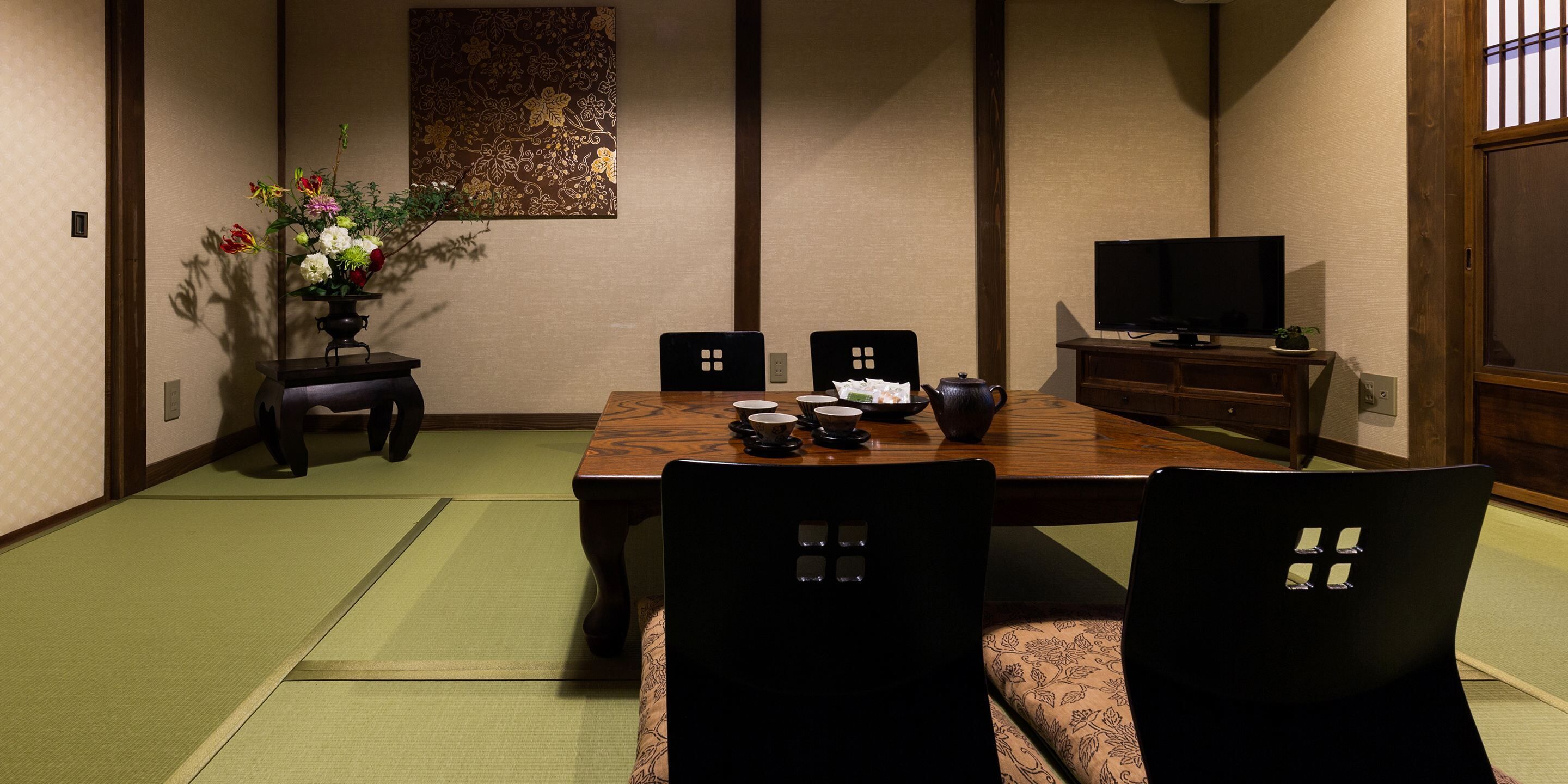 Un comedor tradicional japonés con suelo de tatami, una mesa baja y sillas negras con respaldo recortado.