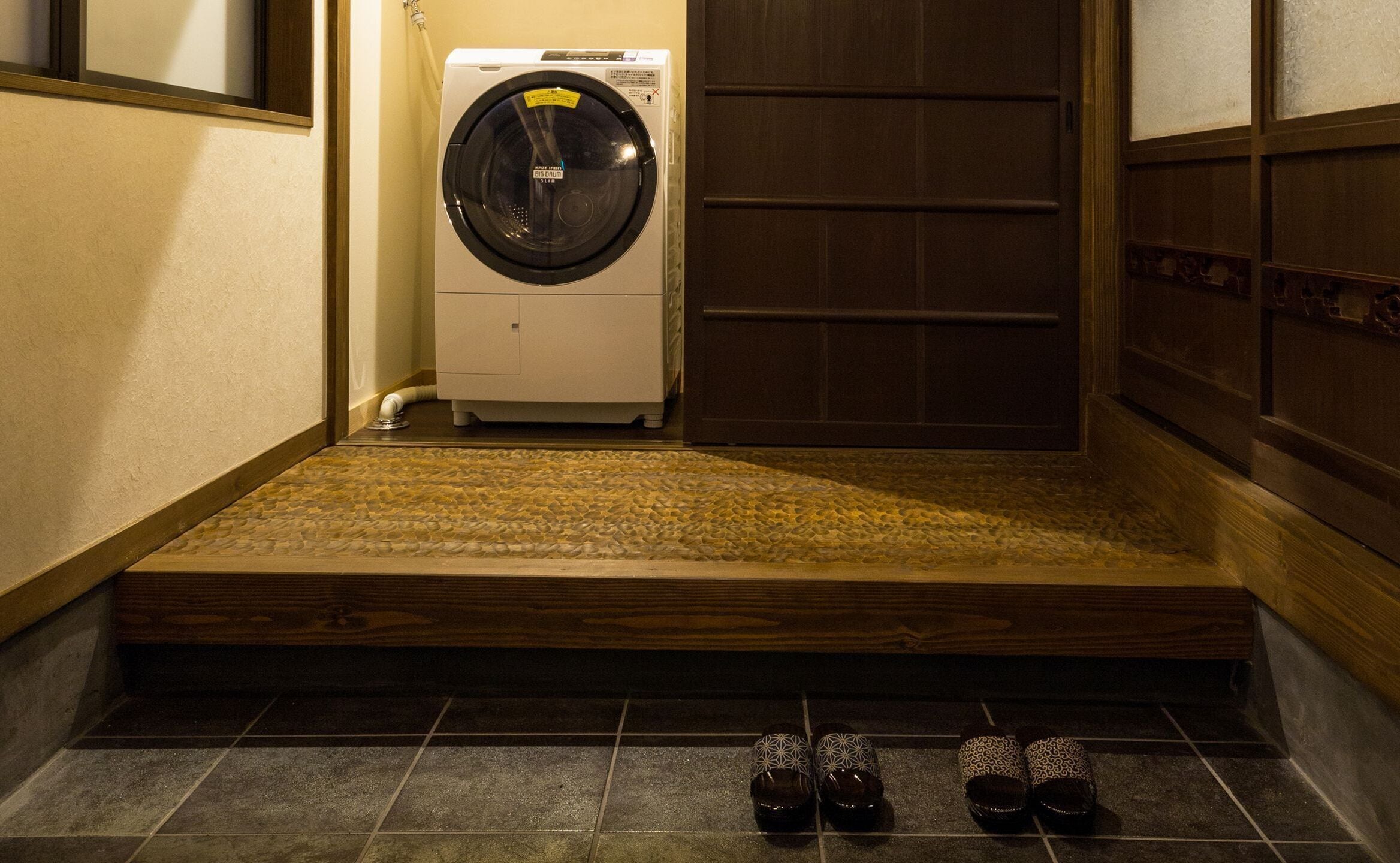 A laundry room with a washing machine, a wooden door, and a tiled floor.
