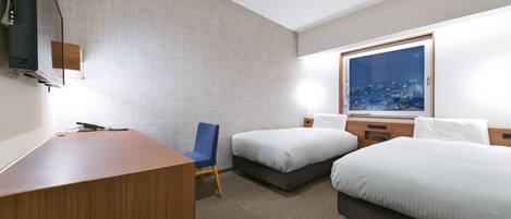 Une chambre d’hôtel équipée d’un bureau, de deux lits simples, d’une chaise, d’une télévision et d’une grande fenêtre donnant sur la ville.