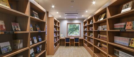 Una biblioteca con estanterías de madera, suelo alfombrado y ventana con vista a árboles.