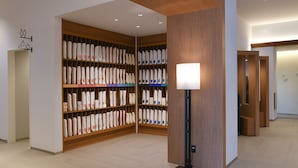 Un pasillo amplio con estanterías de madera repletas de toallas y ropa de cama ordenadas. Una lámpara de pie ofrece iluminación, y el espacio presenta un diseño moderno y limpio con techo de madera y paredes blancas.