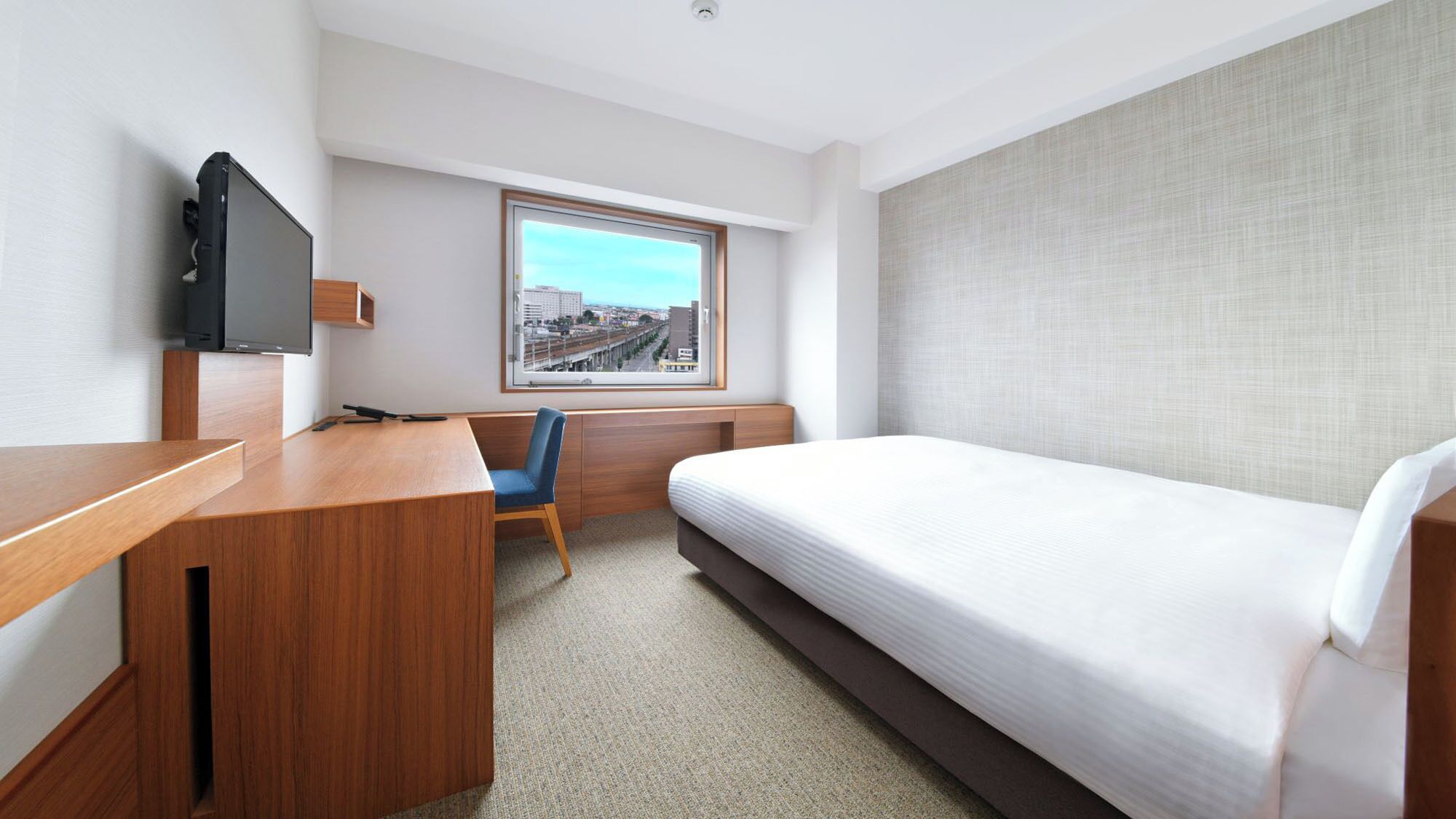 A hotel room with a bed, a desk, a chair, a television, and a window with a city view.