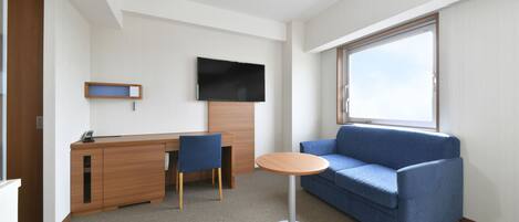 A modern hotel room with a wooden desk, a blue sofa, a round table, and a TV mounted on the wall.