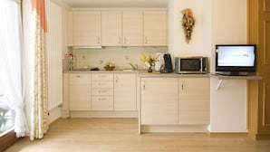 A kitchen with light wood cabinets, a microwave, a television, and a small countertop area with a vase of flowers. - Ferienwohnungen Christl (Reit im Winkl)