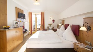 A hotel room with a large bed, wooden wardrobe, bedside table, and a small table with a lamp. - Ferienwohnungen Christl (Reit im Winkl)