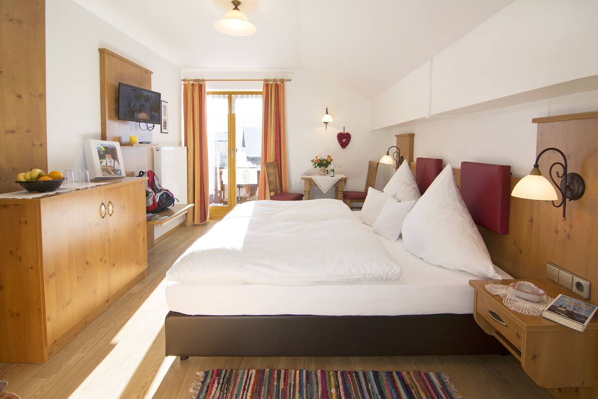 A hotel room with a large bed, wooden wardrobe, bedside table, and a small table with a lamp.