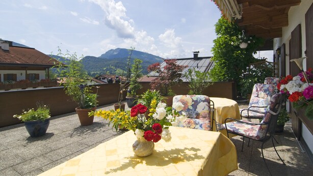 A terrace with a table and chairs, potted plants, and a mountain view. - Ferienwohnungen Christl (Reit im Winkl)