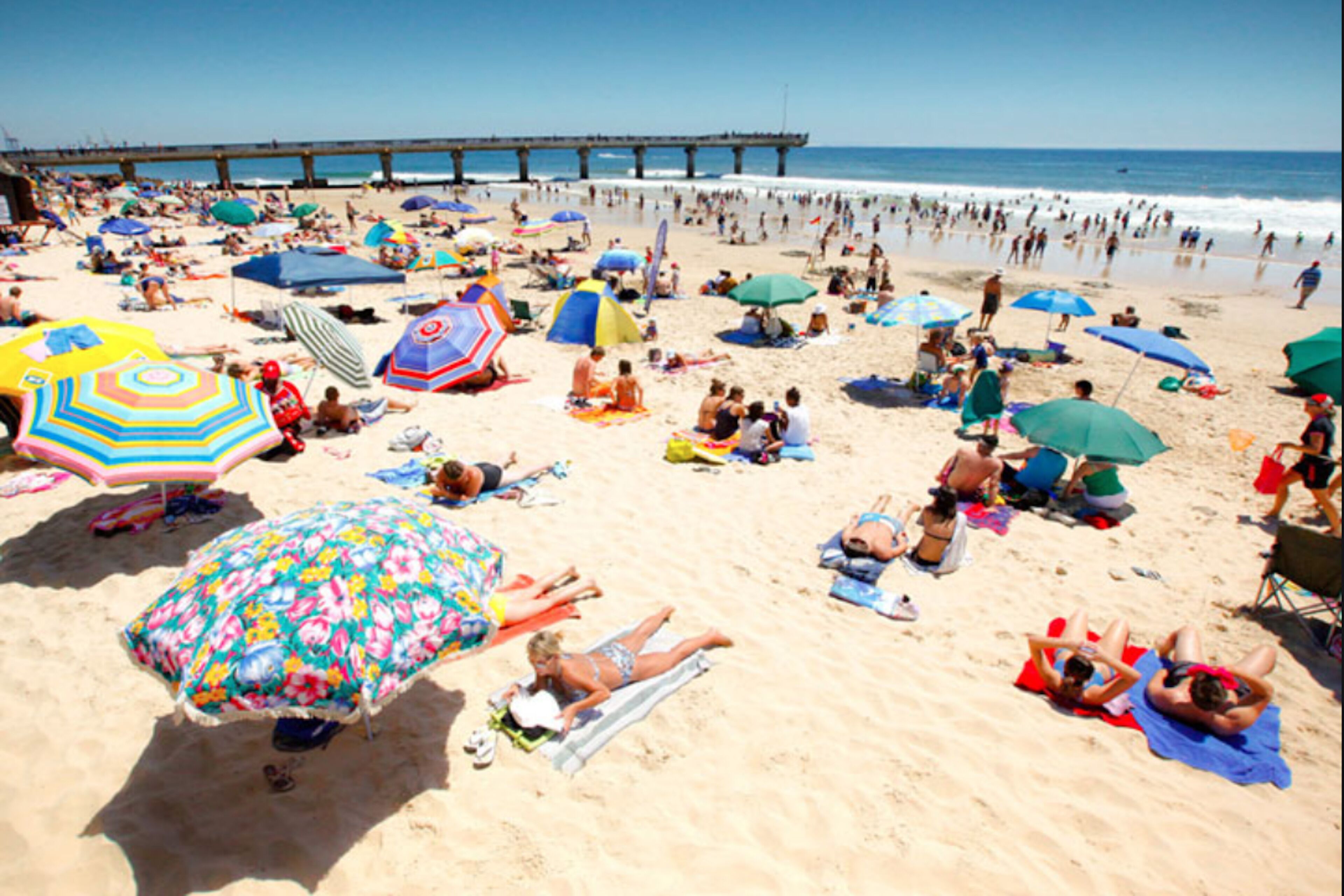 Una playa concurrida, con muchos sombrillas y gente relajándose.