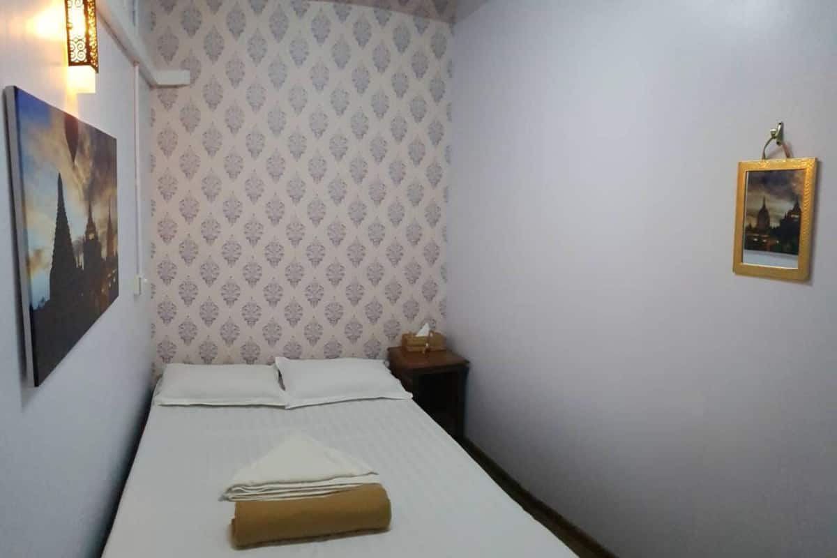 A small, neatly made room with a bed, a nightstand, and a wall-mounted picture.