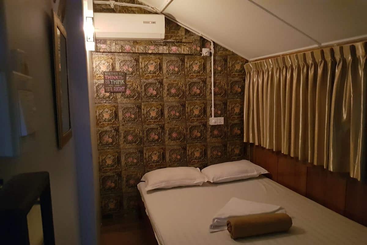 A hotel room with a bed, a window with curtains, a wall with a floral pattern, and an air conditioning unit.