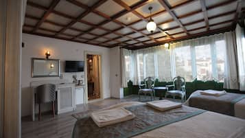 Une chambre d’hôtel avec un plafond en bois, un lit recouvert d’une couverture verte, un bureau avec une chaise et une fenêtre avec des rideaux.