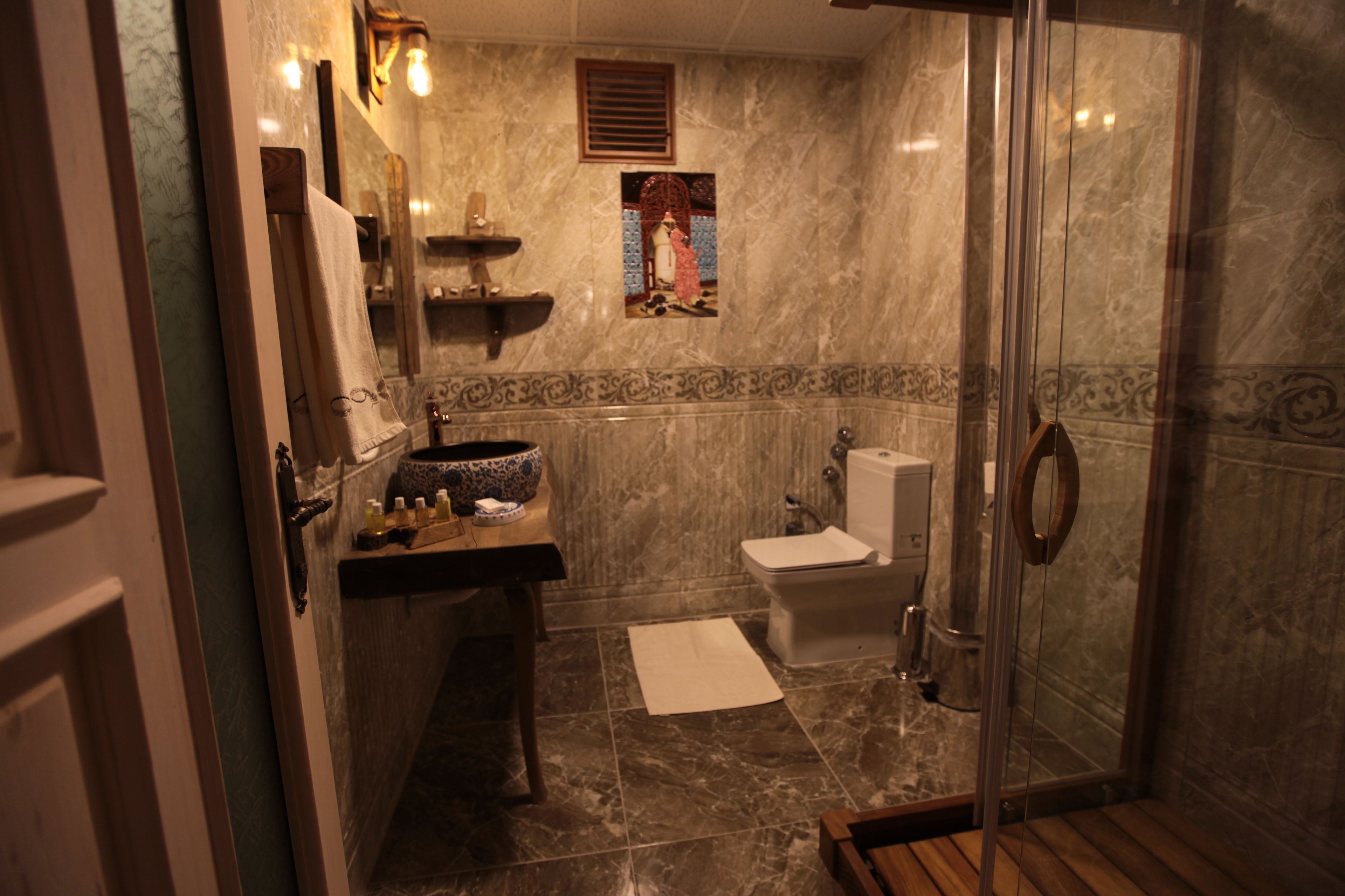 A bathroom with a marble floor, a sink with toiletries, a toilet, and a glass shower enclosure.