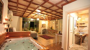 Una habitación amplia con una bañera grande, techo de madera, pared de piedra y vistas a través de un ventanal.