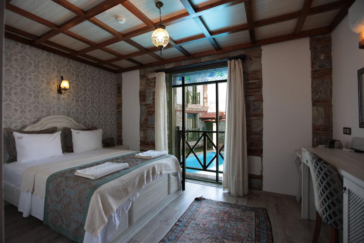 A bedroom with a bed, a desk, a patterned rug, and a view of a swimming pool through a glass door.