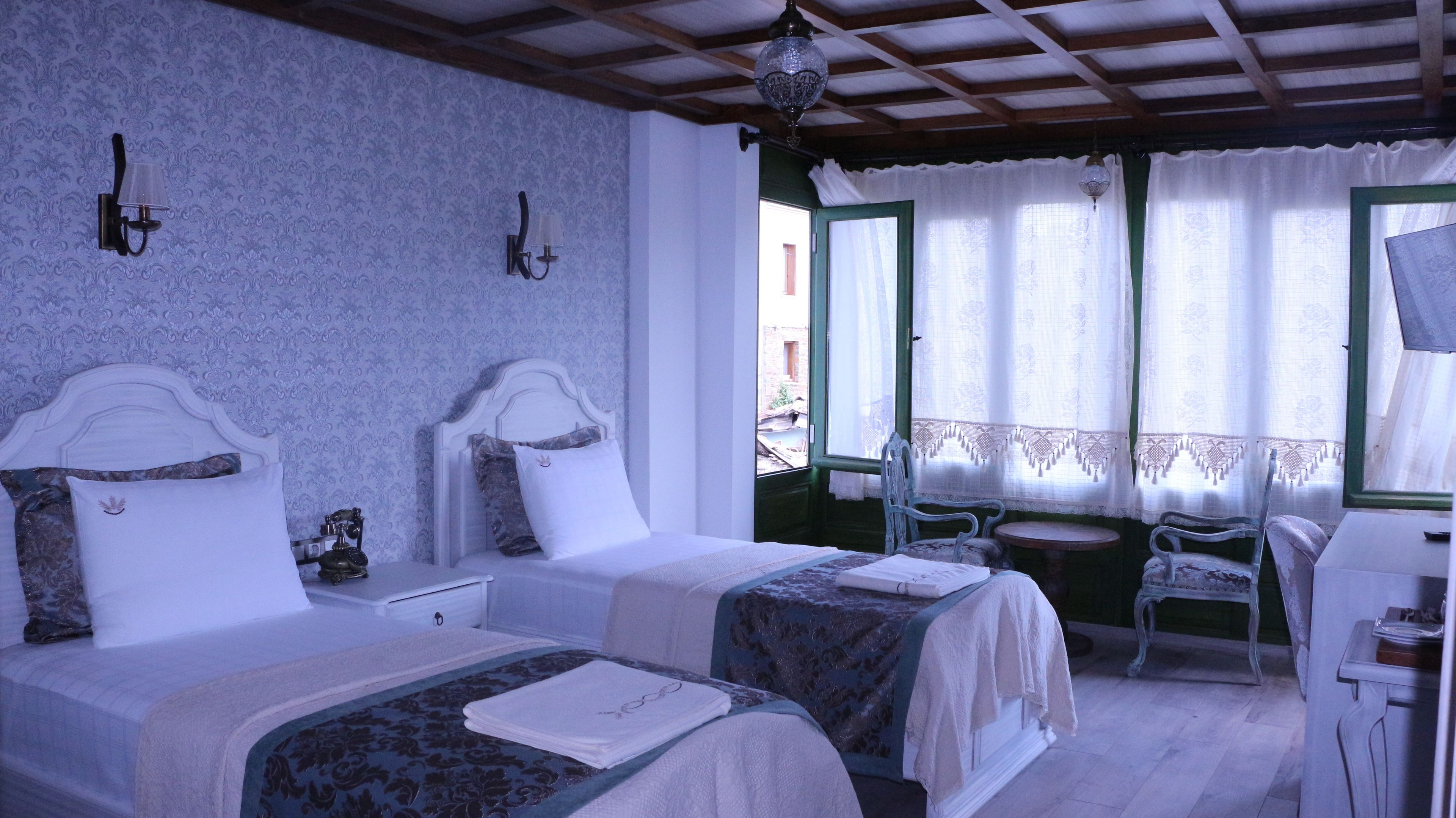 A room with two beds, a small table, a chair, and a window with curtains.
