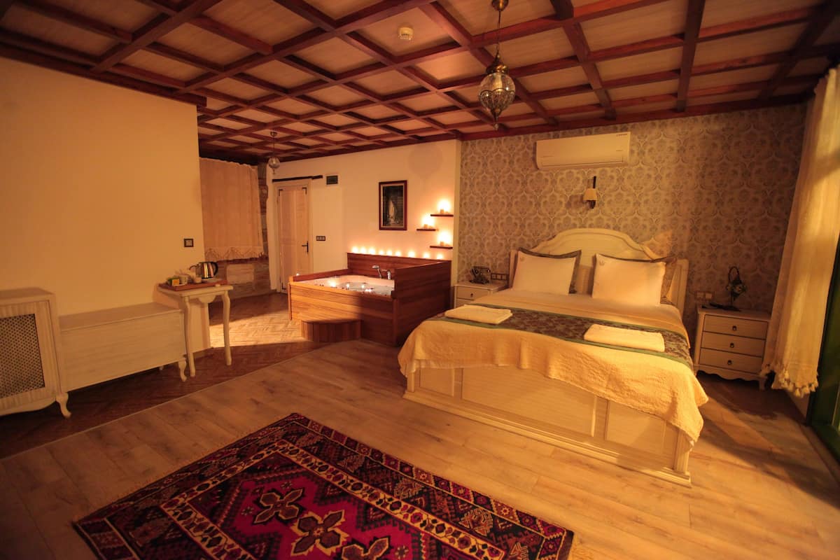 A bedroom with a wooden ceiling, a bed with a white headboard, bedside tables, a nightstand, a dresser, and a patterned rug.
