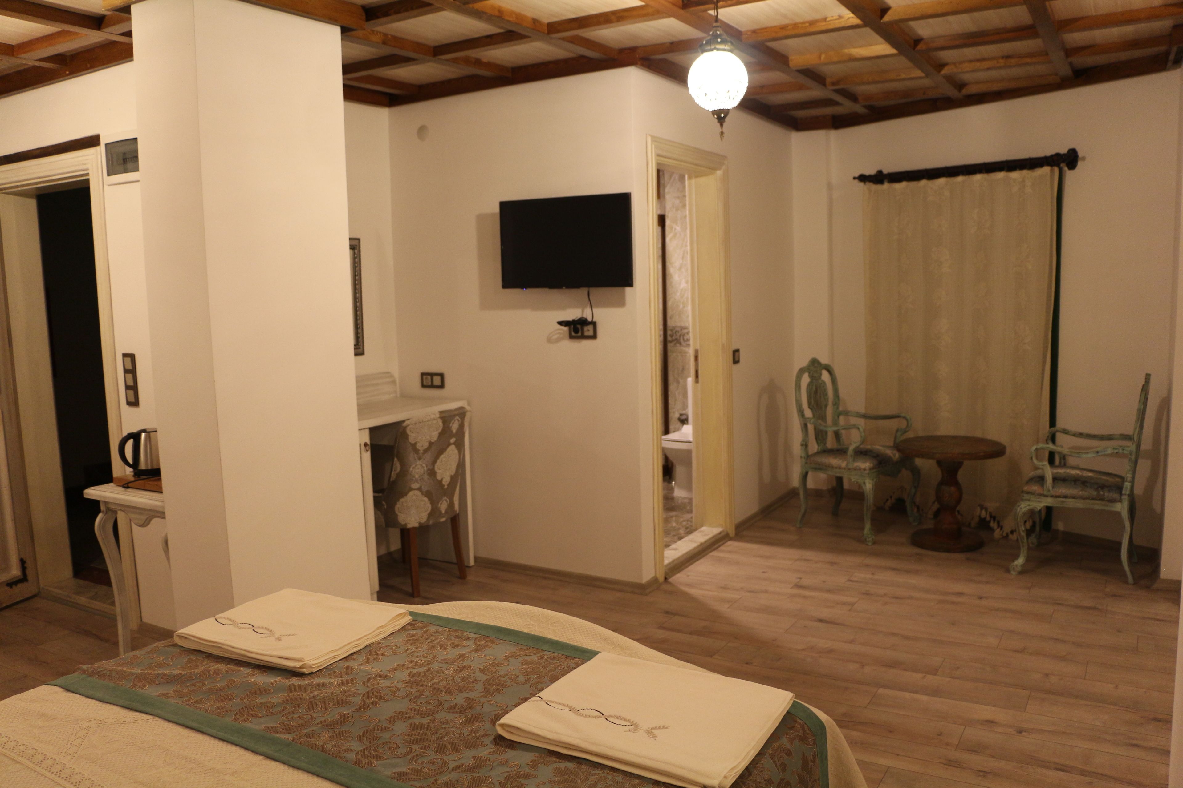 Una habitación con cama, televisión instalada en la pared, mesa y sillas, y techo de madera.
