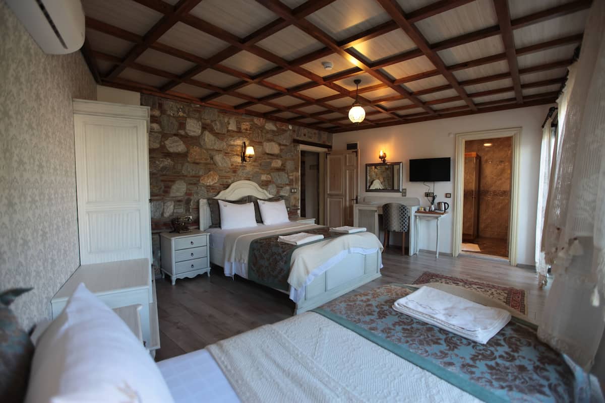 A bedroom with a stone wall, wooden beams, a bed, a desk, a chair, and a TV.