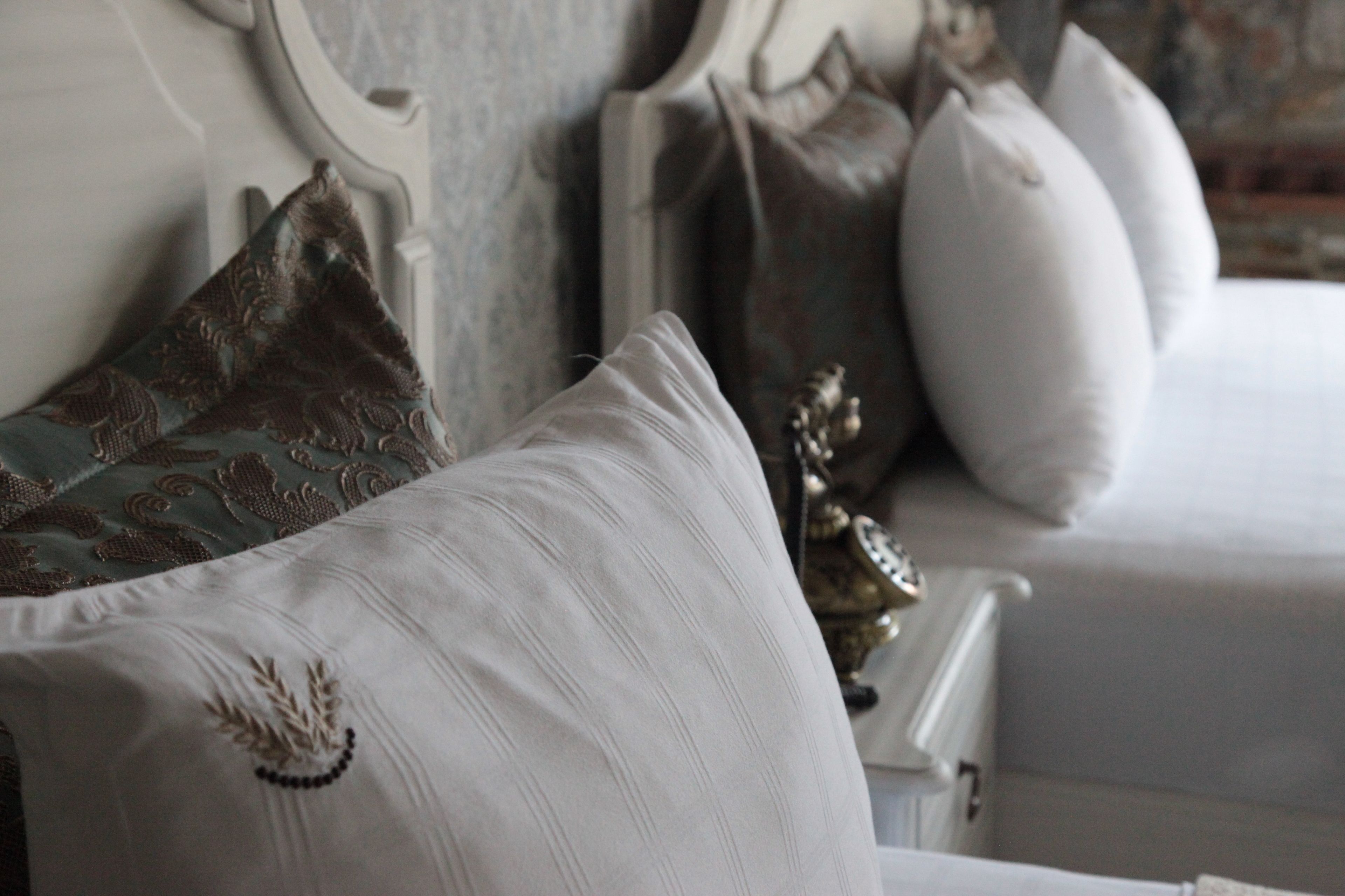 Un letto con cuscini bianchi e decorati, una testiera ornamentale e una piccola statuetta dorata.
