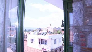 Vista a través de una ventana que muestra un edificio con techo de tejas rojas, un balcón y un muro de ladrillo.