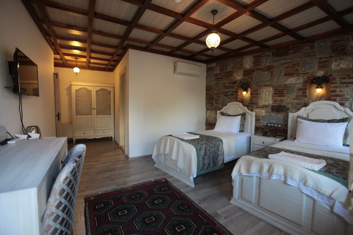 A bedroom with two beds, a wooden ceiling, stone wall, and a television on the wall.