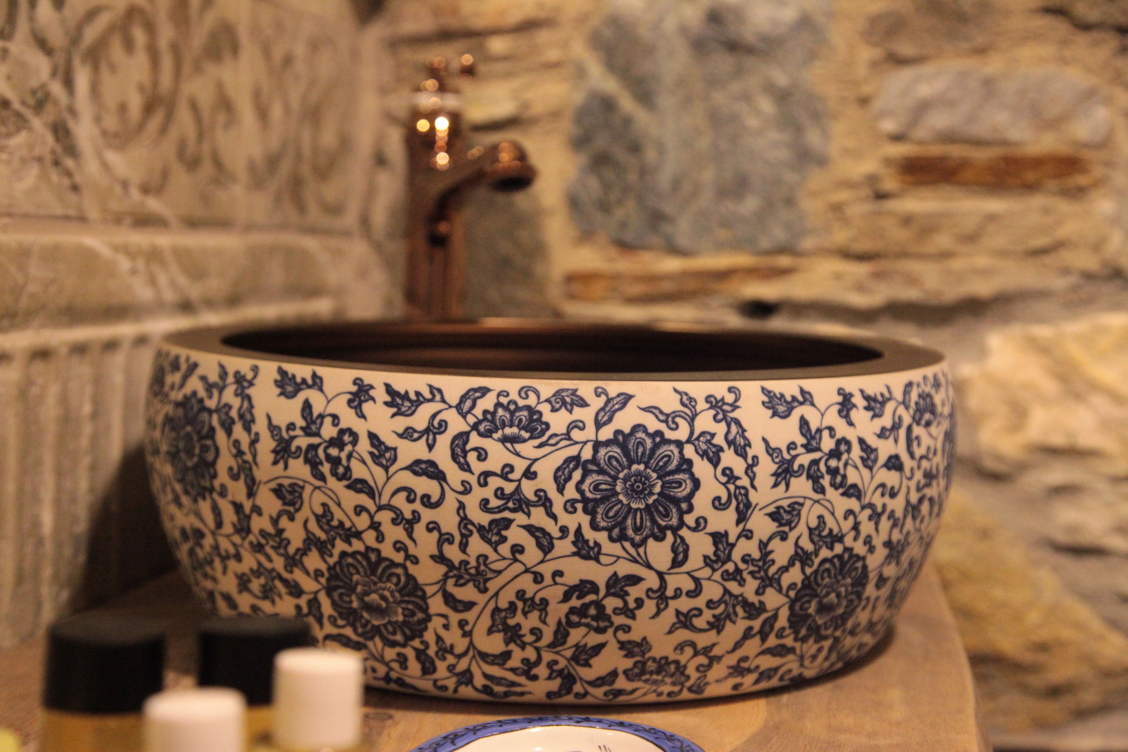 A bathroom with a large, ornate ceramic sink with floral patterns, a stone wall, and a faucet.
