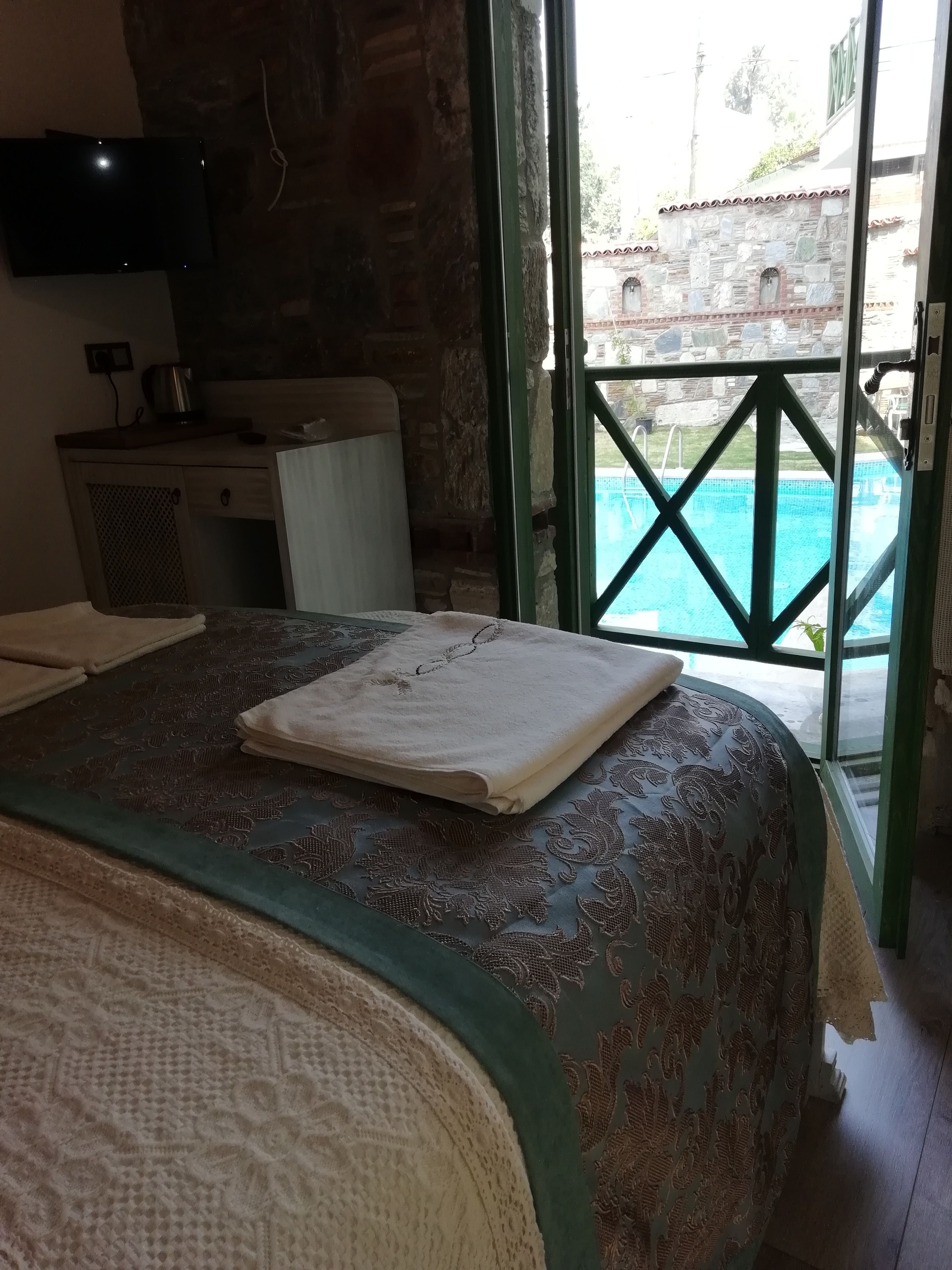 A hotel room with a bed, a desk, a television, and a view of a swimming pool.