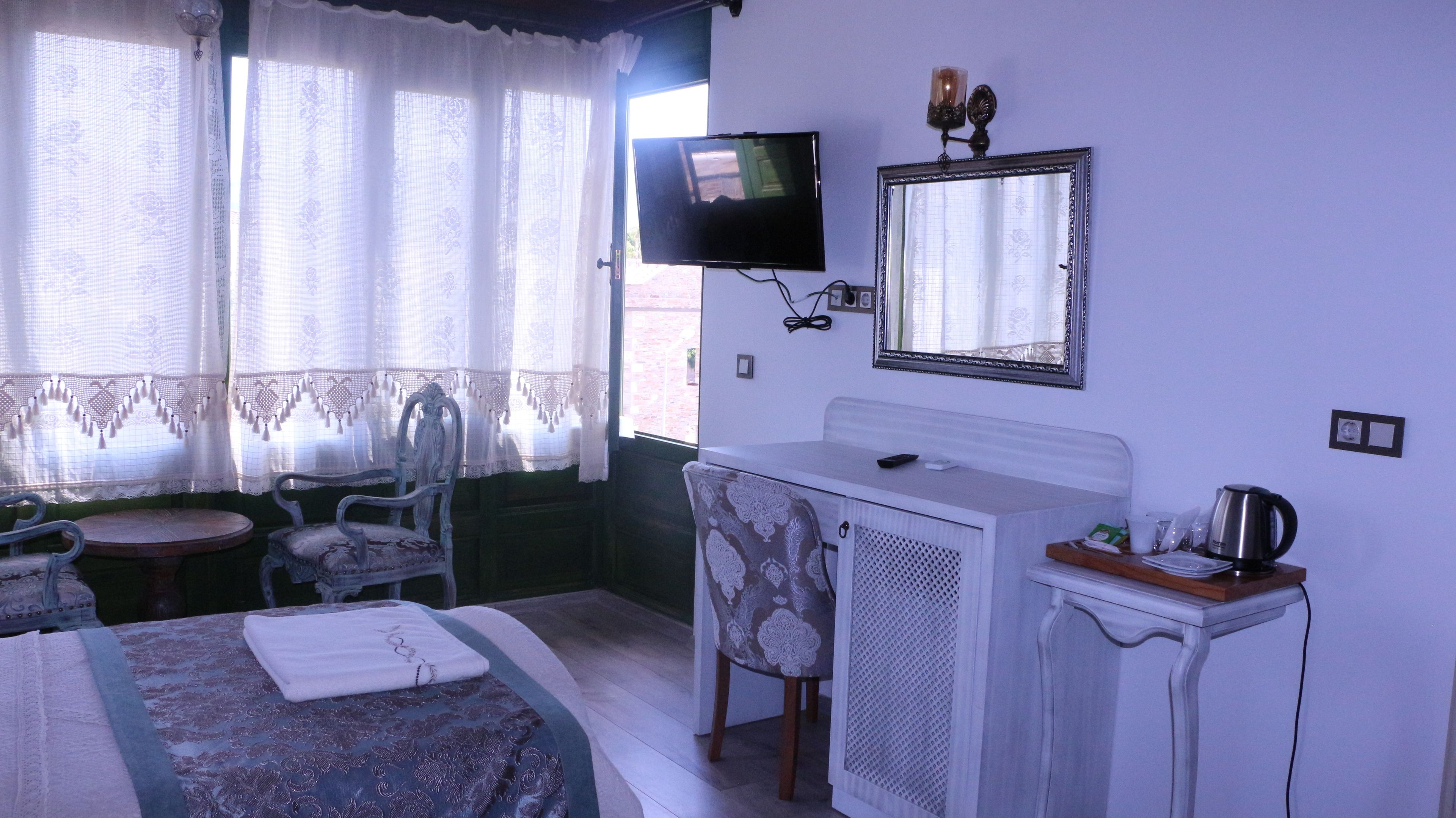 Ein Hotelzimmer mit Bett, Schreibtisch, Stuhl, Fernseher, Spiegel und einem Fenster mit Vorhängen.